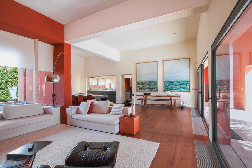 Modelo de sala de estar abierta contemporánea con paredes rojas, suelo de madera en tonos medios, suelo marrón y alfombra