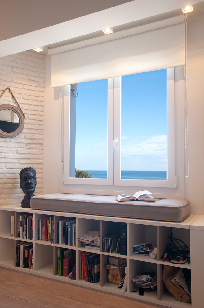 На фото: открытая гостиная комната среднего размера в морском стиле с с книжными шкафами и полками, белыми стенами, полом из ламината, телевизором на стене и коричневым полом