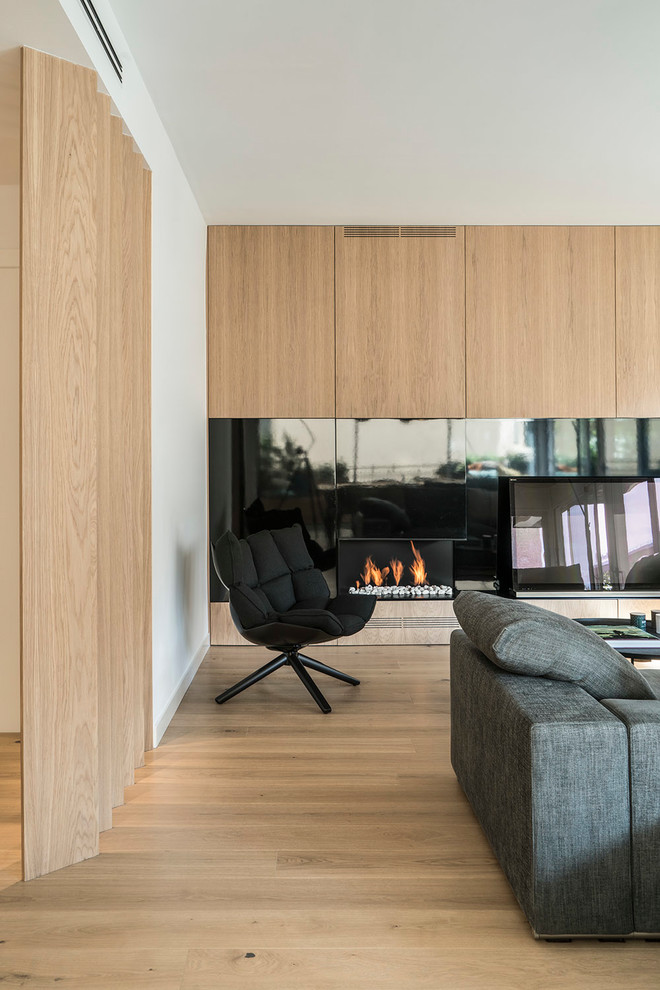 Aménagement d'une salle de séjour contemporaine de taille moyenne et ouverte avec un mur blanc, un sol en bois brun, une cheminée double-face et un téléviseur encastré.