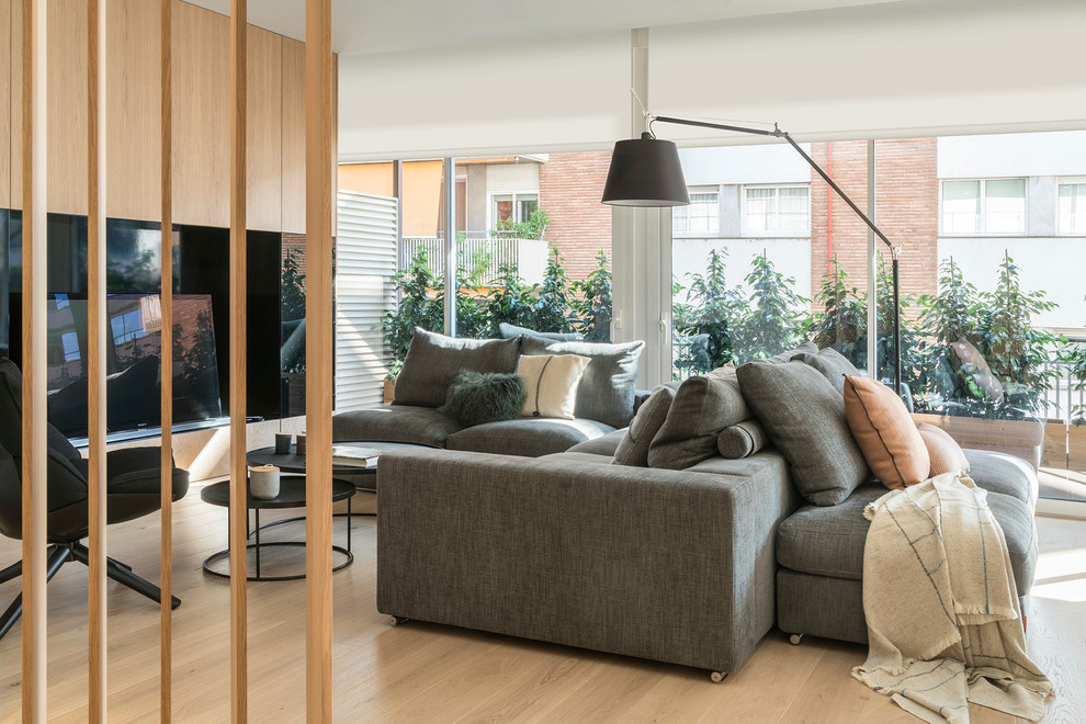 Modelo de sala de estar abierta actual de tamaño medio con paredes blancas, suelo de madera en tonos medios, chimenea de doble cara y pared multimedia