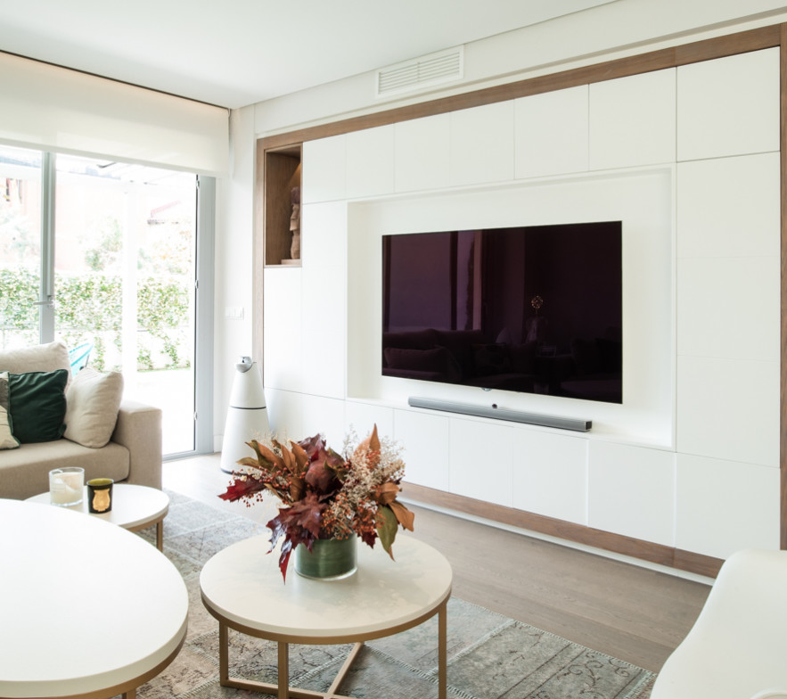 Modern inredning av ett stort allrum med öppen planlösning, med vita väggar, mellanmörkt trägolv, en väggmonterad TV och beiget golv