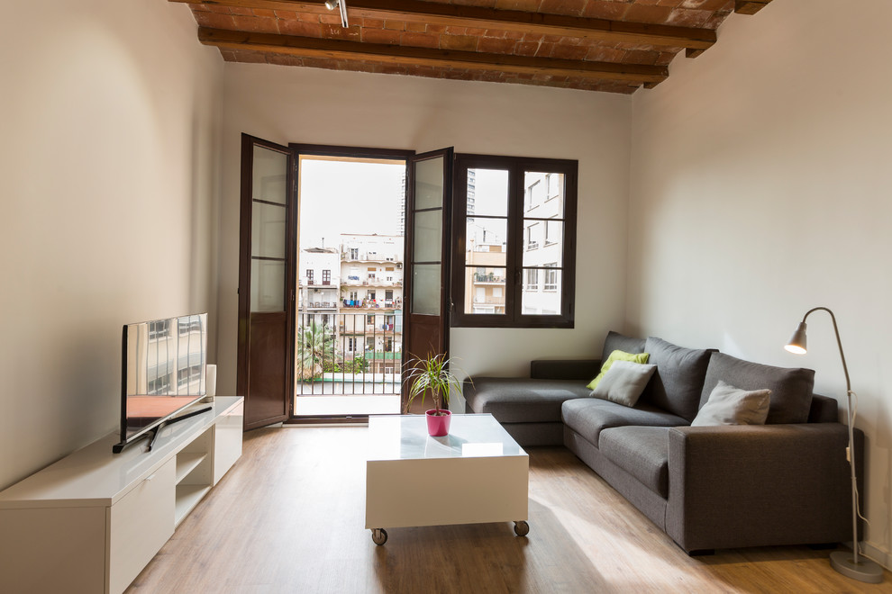 Cette image montre une petite salle de séjour méditerranéenne ouverte avec un mur blanc et un sol en bois brun.