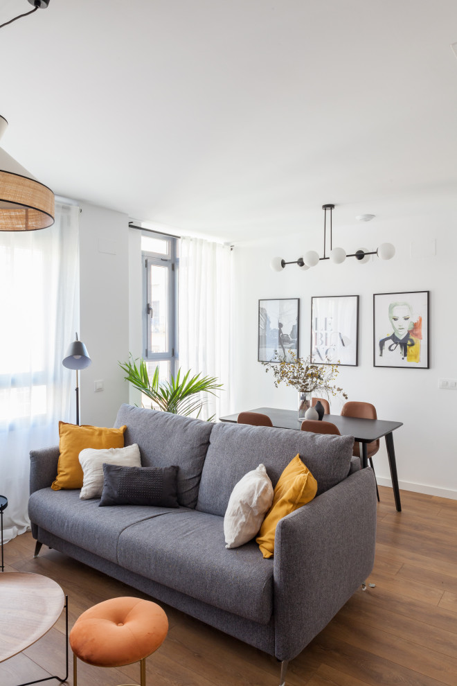 Imagen de sala de estar abierta actual de tamaño medio con paredes blancas, suelo de madera en tonos medios, televisor independiente y suelo marrón