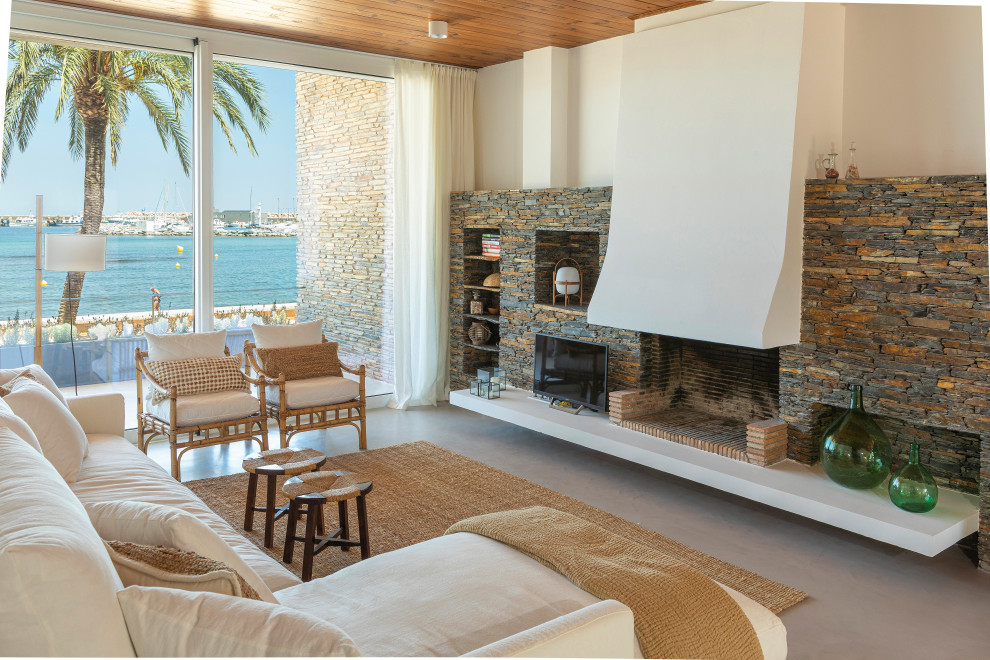 Ejemplo de sala de estar abierta mediterránea extra grande con paredes blancas, suelo de cemento, todas las chimeneas, marco de chimenea de piedra y suelo gris