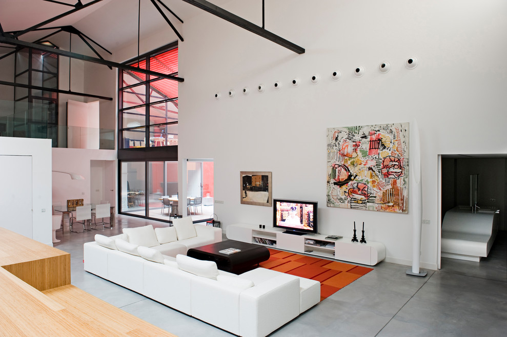 Bild på ett industriellt allrum med öppen planlösning, med vita väggar, betonggolv, en fristående TV och grått golv