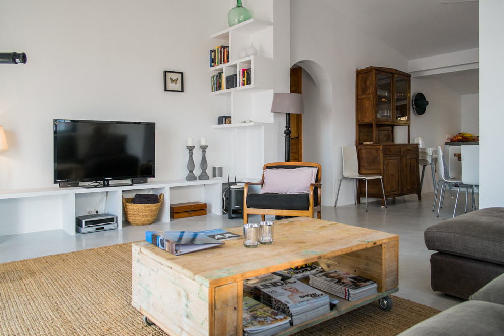 На фото: изолированная гостиная комната среднего размера в средиземноморском стиле с белыми стенами, бетонным полом и отдельно стоящим телевизором без камина с