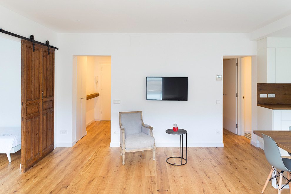 Modelo de sala de estar abierta nórdica de tamaño medio sin chimenea con paredes blancas, suelo de madera clara, televisor colgado en la pared y suelo marrón