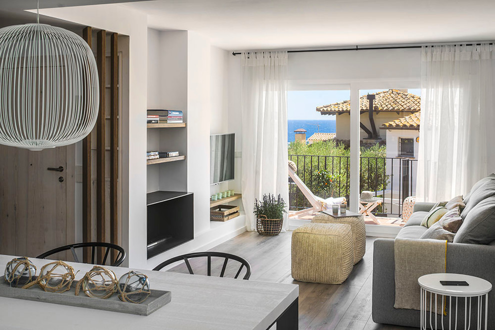 Diseño de sala de estar abierta mediterránea pequeña con paredes blancas, suelo de madera en tonos medios, chimenea lineal y televisor colgado en la pared