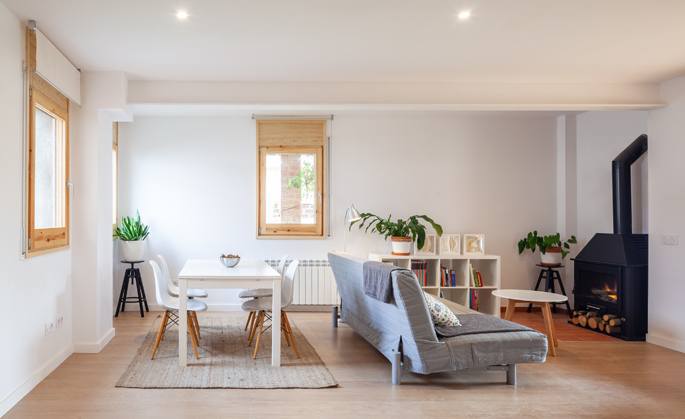 Imagen de sala de estar abierta actual pequeña sin televisor con paredes blancas, suelo de madera clara, estufa de leña y suelo beige