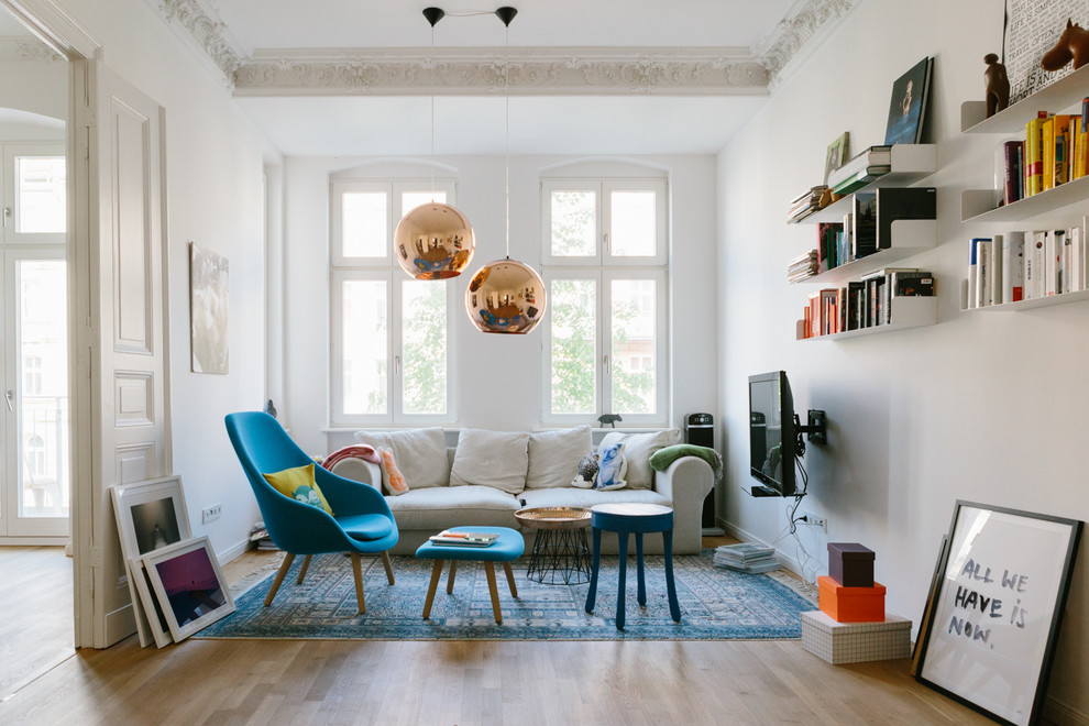Diseño de sala de estar con biblioteca abierta ecléctica de tamaño medio con paredes blancas, suelo de madera en tonos medios y televisor colgado en la pared