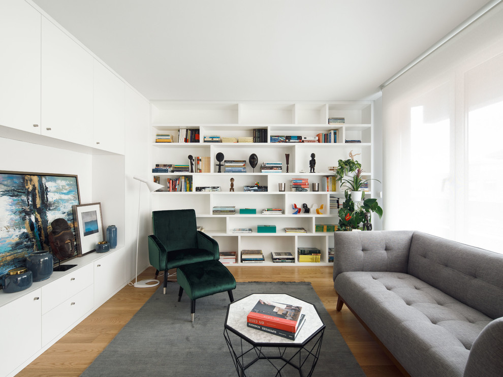На фото: гостиная комната в скандинавском стиле с с книжными шкафами и полками, белыми стенами и светлым паркетным полом без камина, телевизора