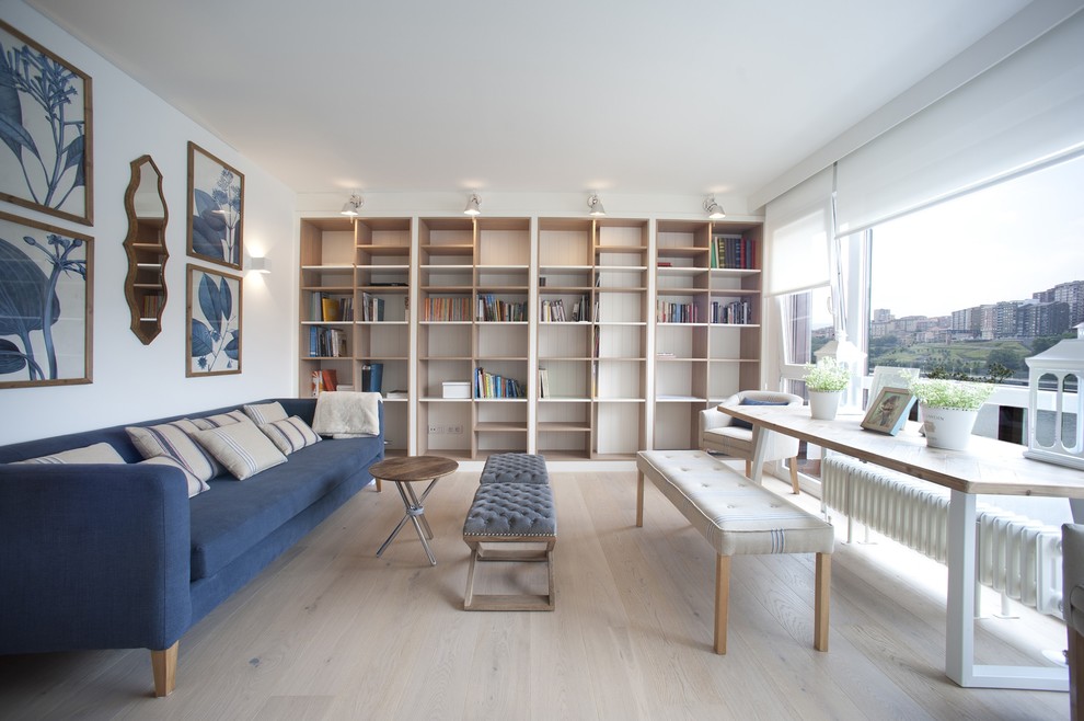 Modelo de sala de estar con biblioteca abierta marinera grande sin chimenea y televisor con paredes blancas, suelo de madera clara y suelo marrón