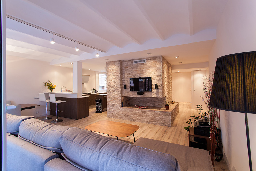 This is an example of a medium sized contemporary open plan games room in Barcelona with beige walls, light hardwood flooring, a ribbon fireplace, a stone fireplace surround, a wall mounted tv and beige floors.