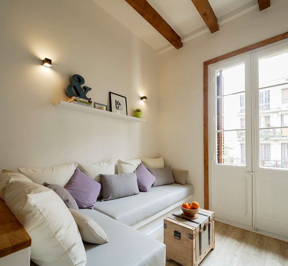 Modelo de sala de estar abierta escandinava pequeña sin chimenea con paredes blancas, suelo de madera clara, televisor colgado en la pared y suelo marrón