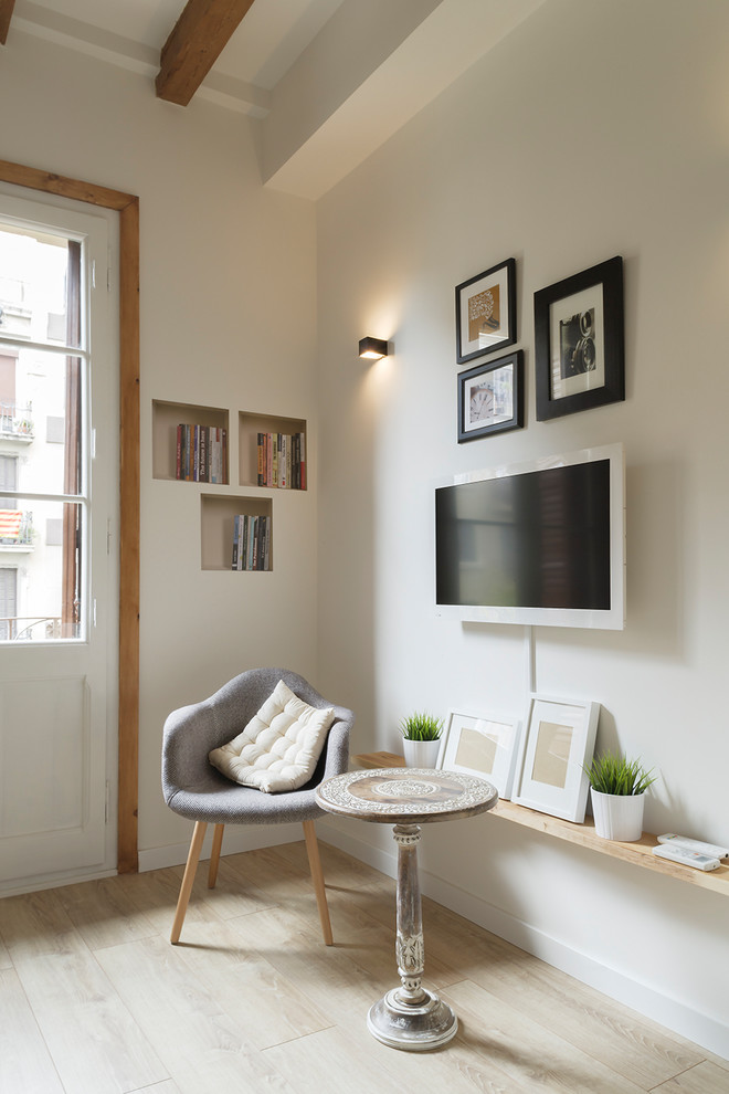 Imagen de sala de estar abierta escandinava pequeña sin chimenea con paredes blancas, suelo de madera clara, televisor colgado en la pared y suelo marrón