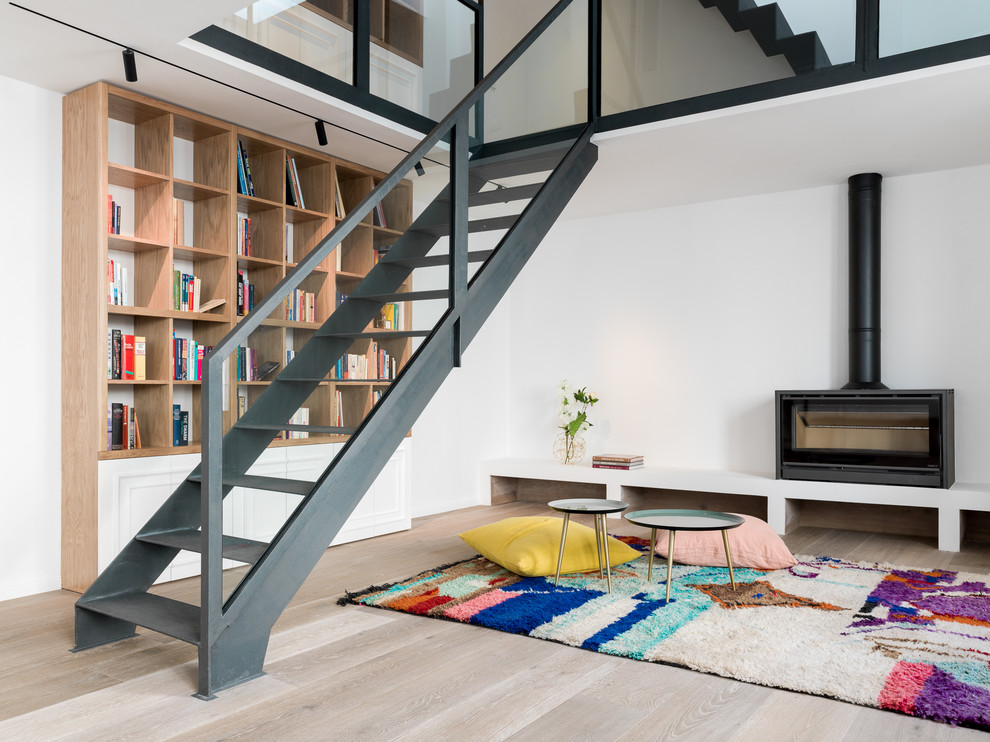 Diseño de sala de estar con biblioteca abierta costera con paredes blancas, suelo de madera clara y estufa de leña