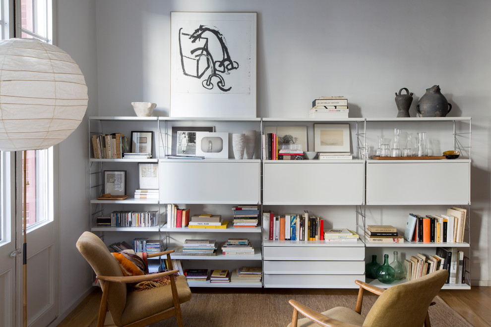 Bild på ett mellanstort minimalistiskt avskilt allrum, med ett bibliotek, vita väggar och mellanmörkt trägolv