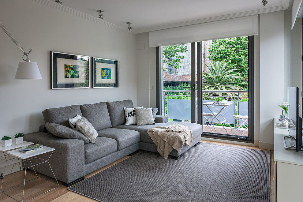 Foto de sala de estar abierta minimalista de tamaño medio con paredes blancas, suelo de madera clara y televisor independiente
