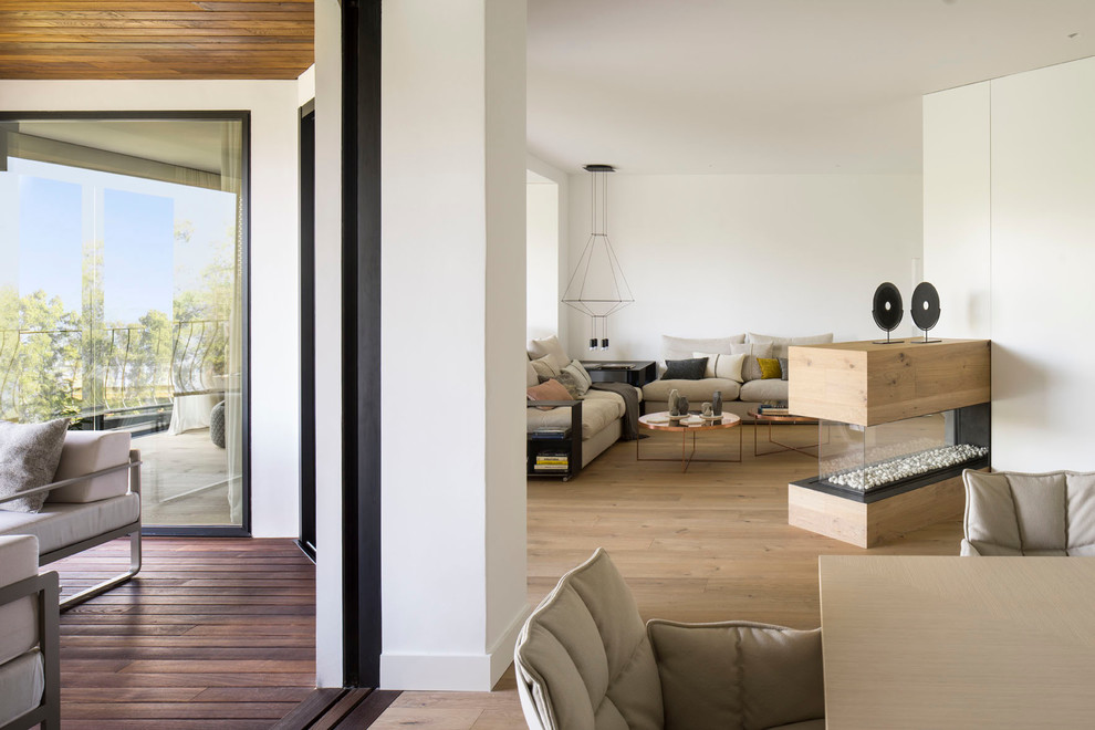 Идея дизайна: большая открытая гостиная комната в современном стиле с белыми стенами, паркетным полом среднего тона, двусторонним камином и фасадом камина из дерева