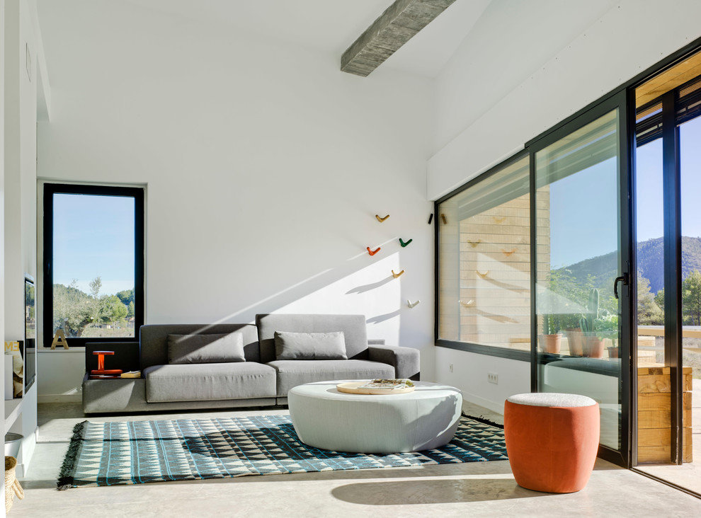 Cette image montre une salle de séjour design de taille moyenne et fermée avec un mur blanc, sol en béton ciré, un téléviseur fixé au mur et aucune cheminée.