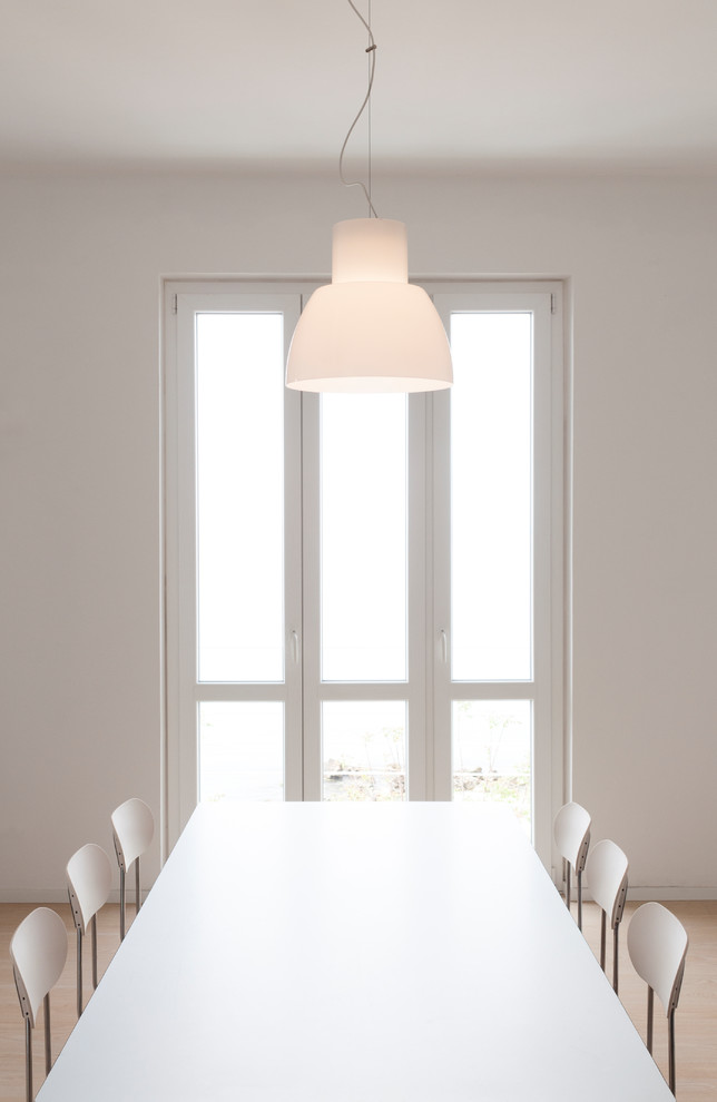 Immagine di una sala da pranzo aperta verso il soggiorno minimalista con pareti bianche e pavimento in laminato