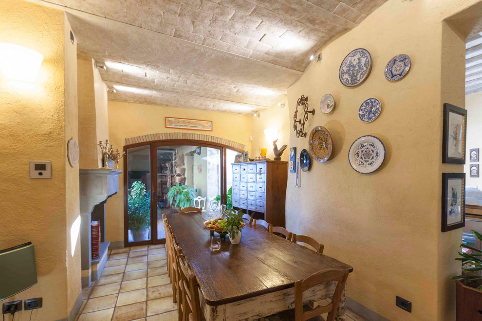 Idée de décoration pour une salle à manger ouverte sur la cuisine champêtre de taille moyenne avec un mur beige, tomettes au sol, une cheminée standard et un manteau de cheminée en pierre.