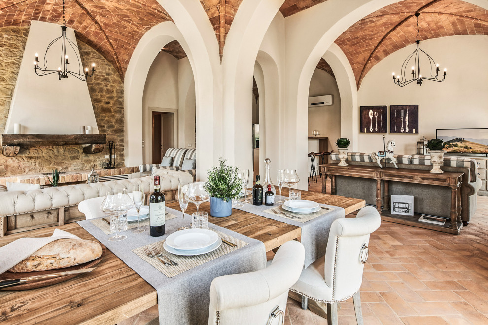 Idée de décoration pour une grande salle à manger ouverte sur le salon méditerranéenne avec un mur beige, tomettes au sol, une cheminée standard, un sol marron et un plafond voûté.