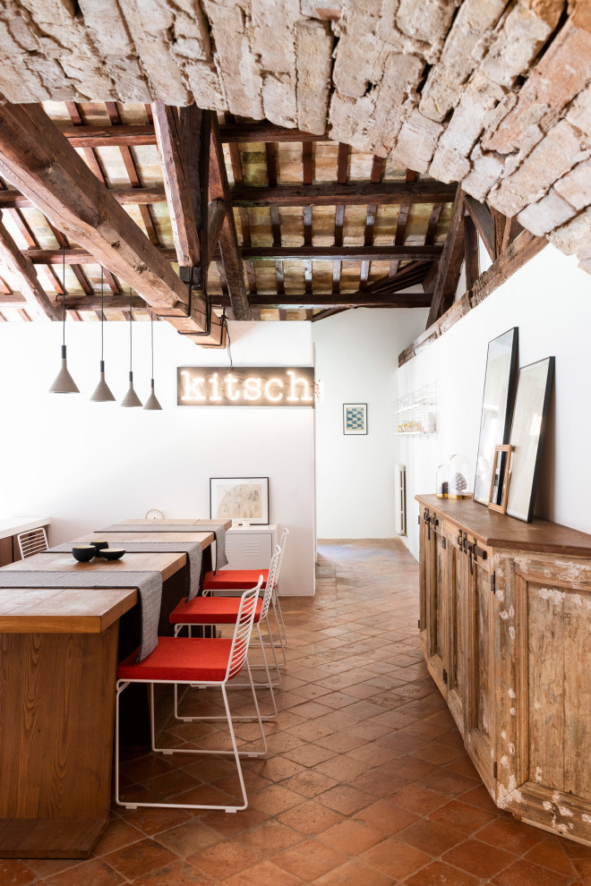 Réalisation d'une très grande salle à manger ouverte sur le salon méditerranéenne avec un mur blanc, poutres apparentes, tomettes au sol et un sol rouge.