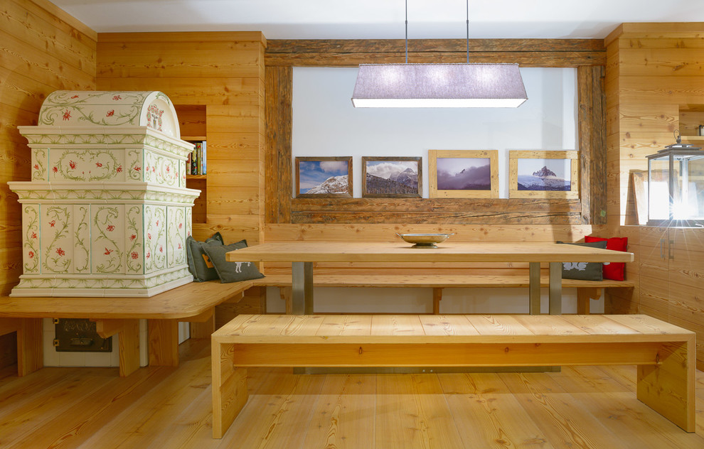 Immagine di una piccola sala da pranzo aperta verso il soggiorno rustica con pareti marroni, parquet chiaro, stufa a legna, cornice del camino piastrellata e pavimento marrone