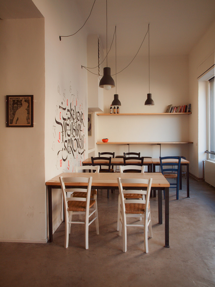 Immagine di un'ampia sala da pranzo aperta verso il soggiorno industriale con pareti bianche e pavimento in cemento