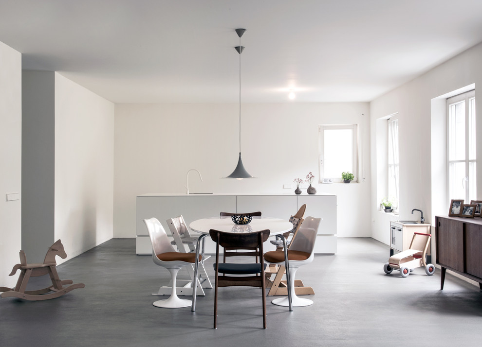 На фото: столовая среднего размера в скандинавском стиле с белыми стенами и бетонным полом с