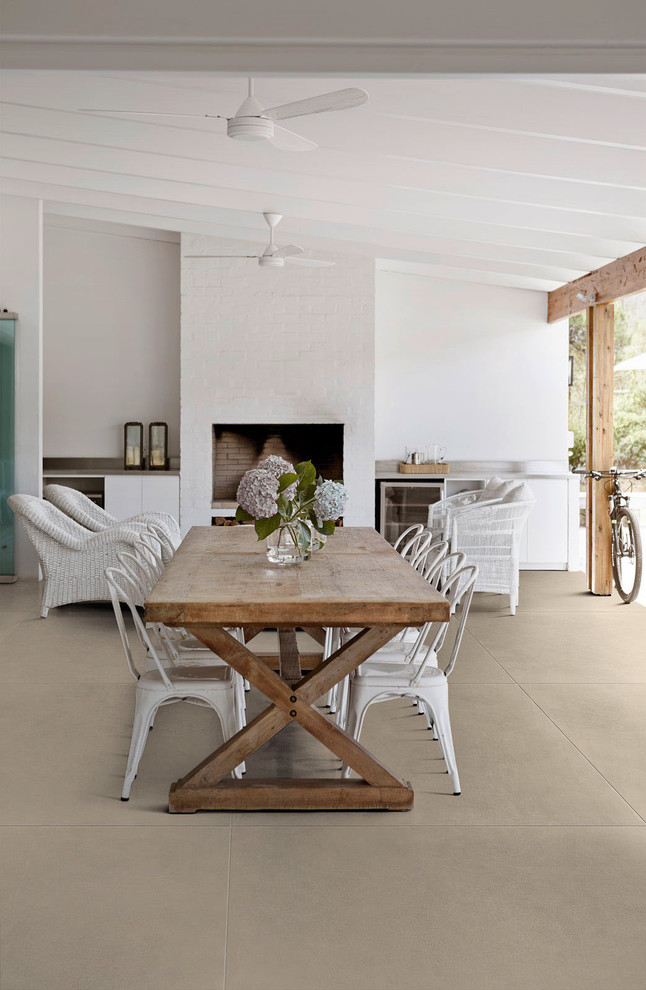 Exemple d'une salle à manger bord de mer avec un sol en carrelage de porcelaine, un mur blanc, une cheminée standard et un sol beige.