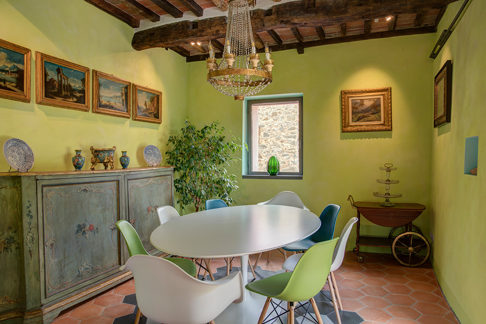 Cette image montre une salle à manger méditerranéenne avec un mur vert, tomettes au sol, aucune cheminée, un sol orange et poutres apparentes.