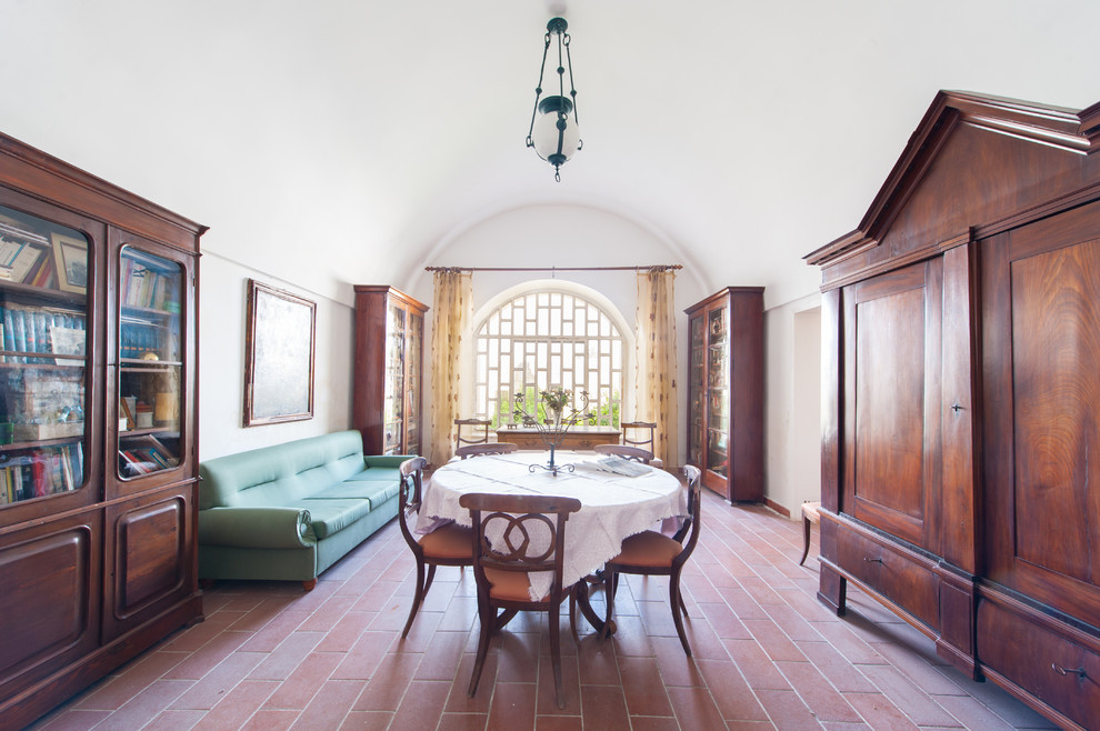 Aménagement d'une salle à manger ouverte sur le salon méditerranéenne avec un mur blanc, tomettes au sol, aucune cheminée et un sol rouge.
