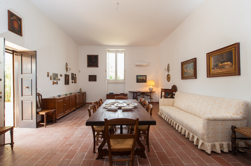 Immagine di una sala da pranzo aperta verso il soggiorno mediterranea con pareti bianche, pavimento in terracotta e pavimento rosso