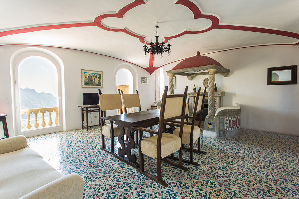 Immagine di una sala da pranzo mediterranea chiusa con pareti bianche, pavimento con piastrelle in ceramica, camino classico e cornice del camino in pietra