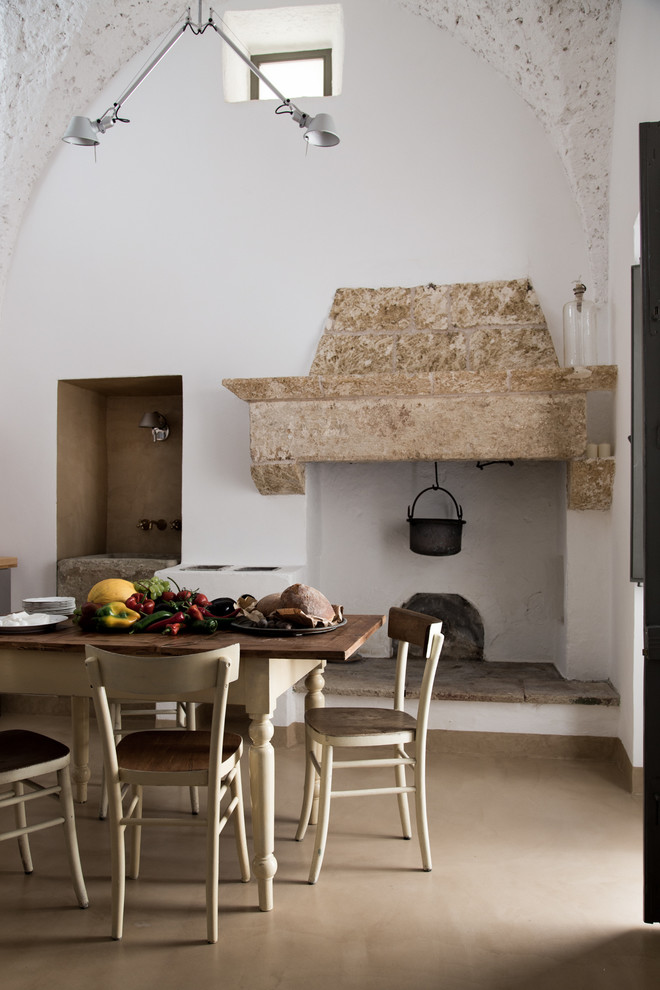 Ejemplo de comedor de cocina de estilo de casa de campo con paredes blancas, suelo de baldosas de porcelana, todas las chimeneas y marco de chimenea de piedra
