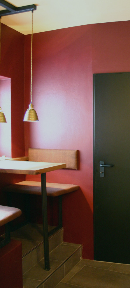 Exemple d'une petite salle à manger industrielle avec une banquette d'angle, un mur rouge, un sol en carrelage de porcelaine et un sol gris.