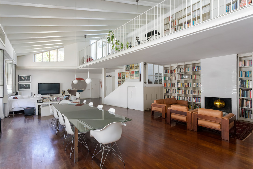 Cette image montre une salle à manger ouverte sur le salon design avec un mur blanc, un sol en bois brun, une cheminée standard, un manteau de cheminée en carrelage et un sol marron.