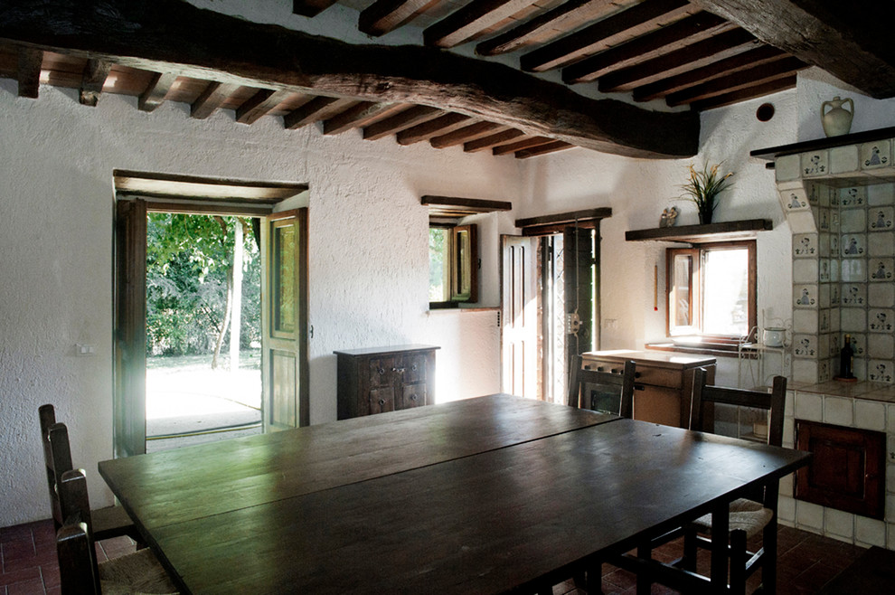 Idée de décoration pour une grande salle à manger ouverte sur la cuisine champêtre avec un mur blanc, tomettes au sol, un poêle à bois, un manteau de cheminée en carrelage et un sol marron.