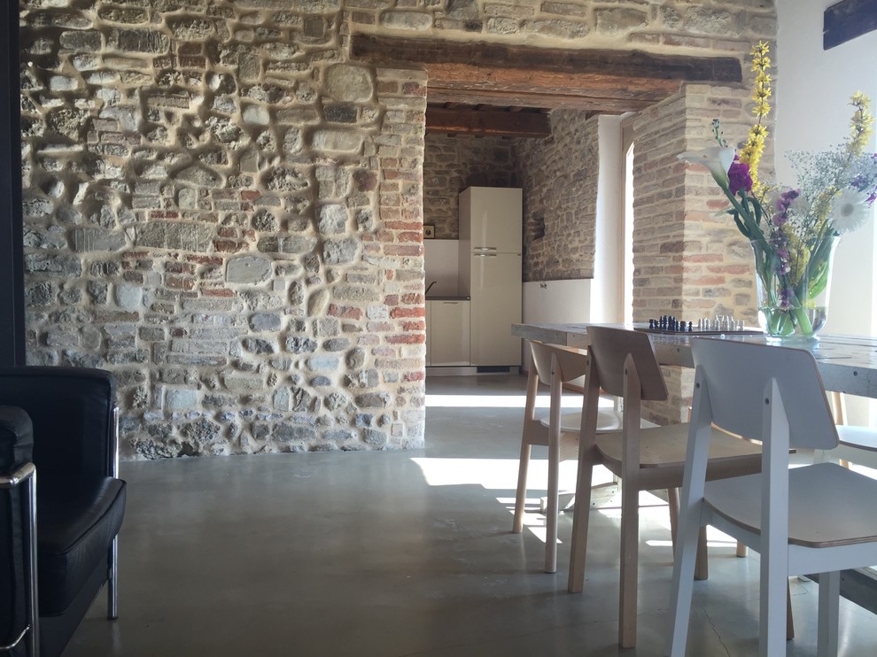Foto di una sala da pranzo aperta verso la cucina country di medie dimensioni con pareti multicolore, pavimento in cemento, camino classico e cornice del camino in mattoni