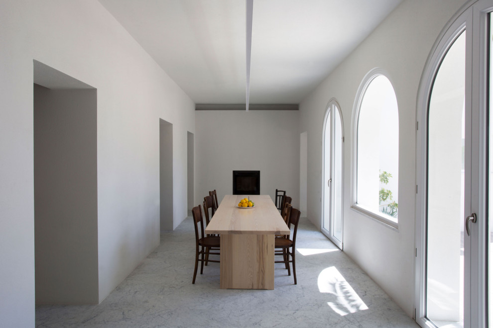 Immagine di una sala da pranzo mediterranea chiusa e di medie dimensioni con pareti bianche, camino classico, cornice del camino in intonaco e pavimento grigio