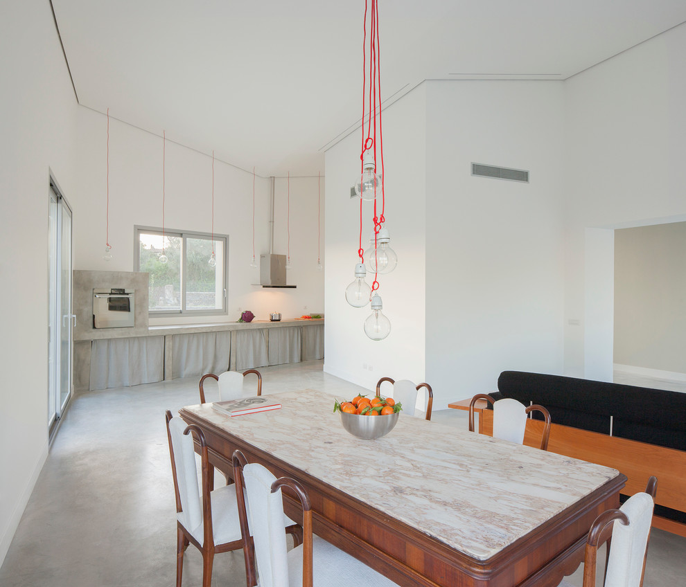 Foto di una sala da pranzo aperta verso la cucina bohémian con pareti bianche e pavimento in cemento