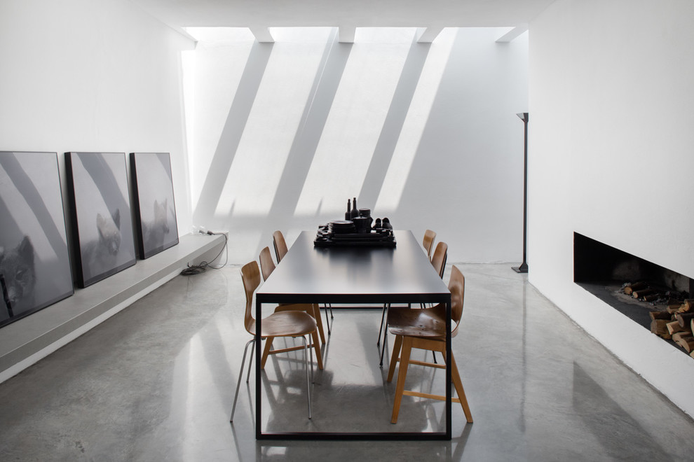 Esempio di una sala da pranzo minimal con pareti bianche, pavimento in cemento e camino classico