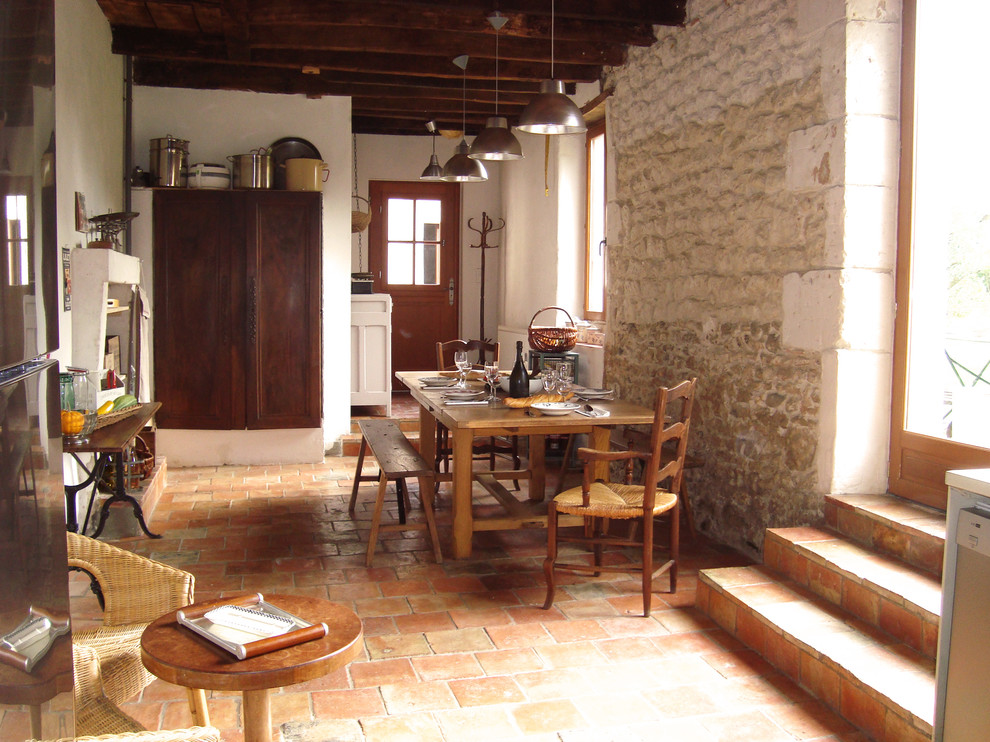 Cette image montre une grande salle à manger ouverte sur le salon rustique avec un mur beige, tomettes au sol et un sol orange.