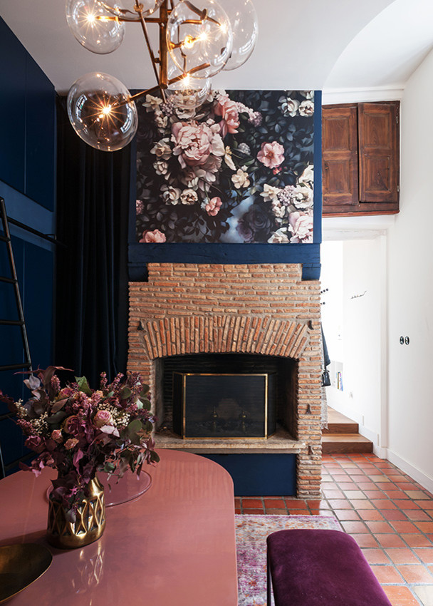 На фото: маленькая гостиная-столовая в стиле фьюжн с синими стенами, полом из терракотовой плитки, стандартным камином, фасадом камина из кирпича и красным полом для на участке и в саду с