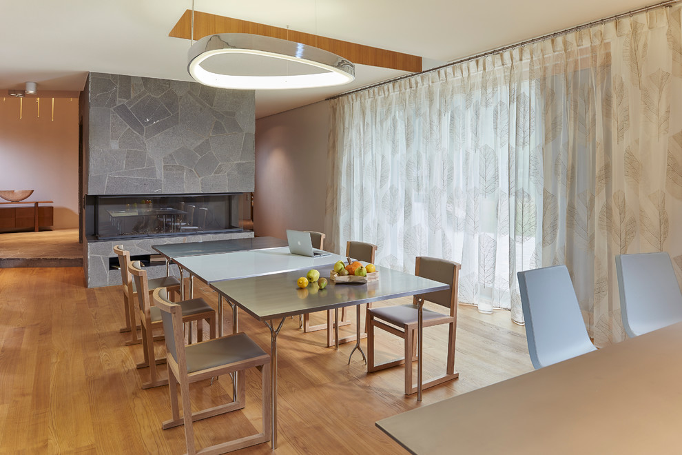 Immagine di una sala da pranzo aperta verso il soggiorno minimal con pareti beige, parquet chiaro, camino lineare Ribbon e cornice del camino in pietra
