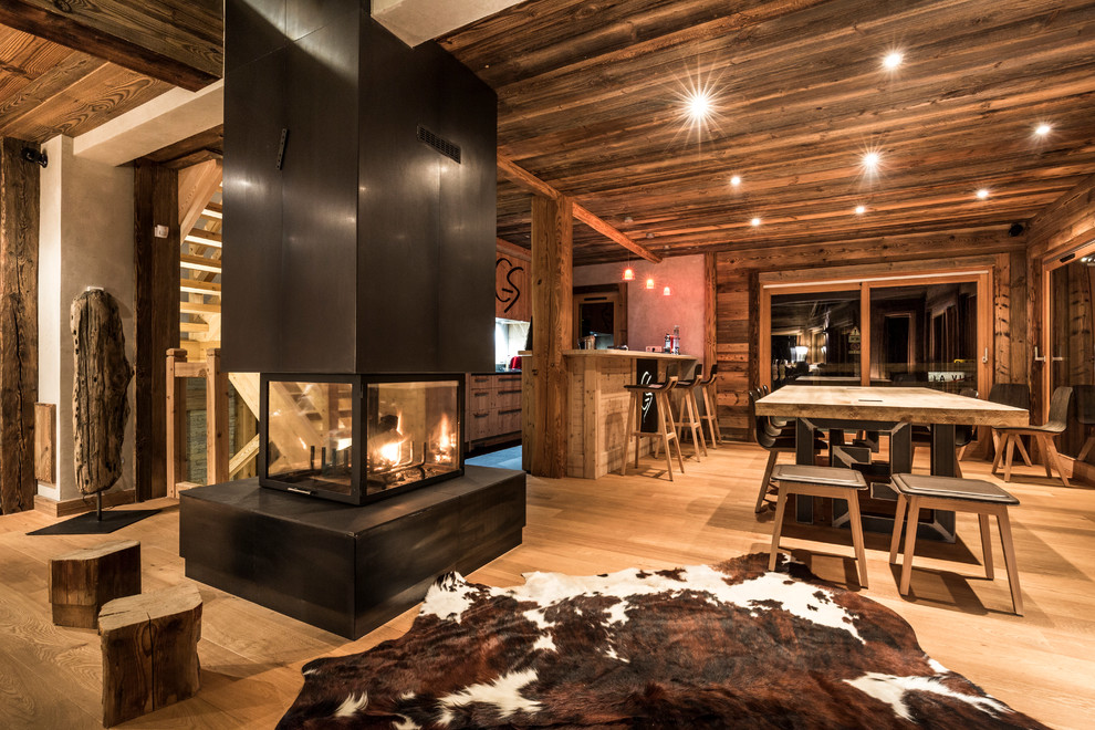 Idées déco pour une grande salle à manger ouverte sur le salon montagne avec un sol en bois brun, une cheminée double-face et un manteau de cheminée en métal.