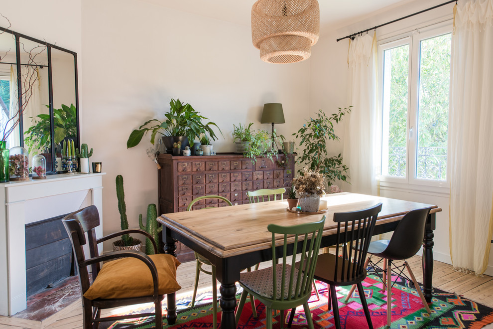 Cette photo montre une salle à manger éclectique avec un mur blanc, parquet clair, une cheminée standard, un sol beige et éclairage.
