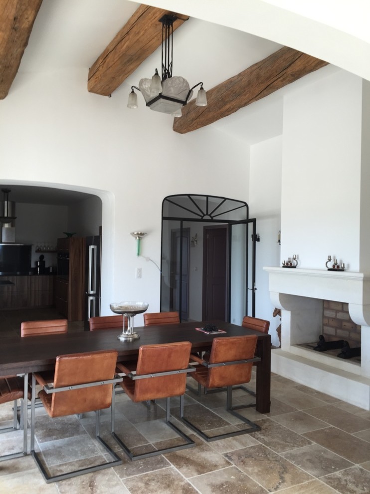 Idée de décoration pour une salle à manger méditerranéenne avec un mur blanc, un sol en travertin, une cheminée standard, un manteau de cheminée en plâtre et un sol marron.